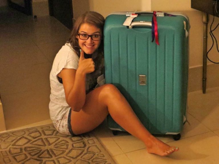 #23 Cómo hacer una mochila minimalista para viajar Mochila minimalista para viajar: yo sentada en el suelo sonriente abrazando mi maleta grande color turquesa